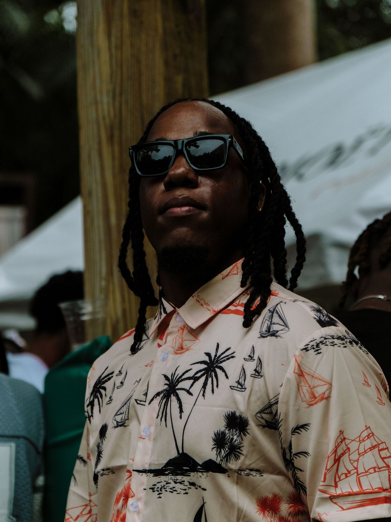 Person in sunglasses and a tropical print shirt enjoying sunny outdoor weather.