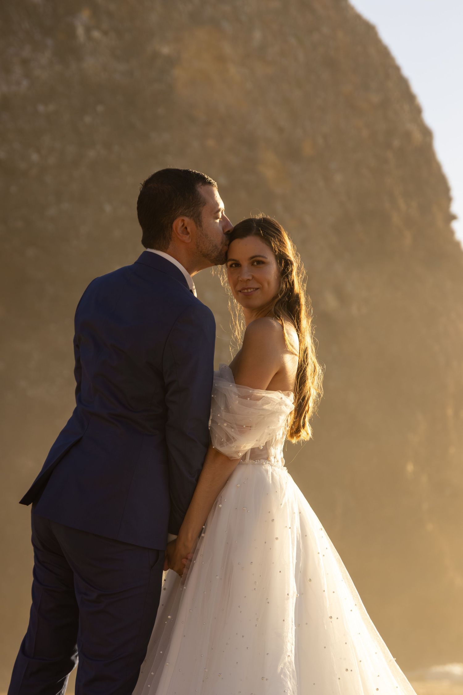Romantic wedding portraits against a misty coastal cliff at golden hour.