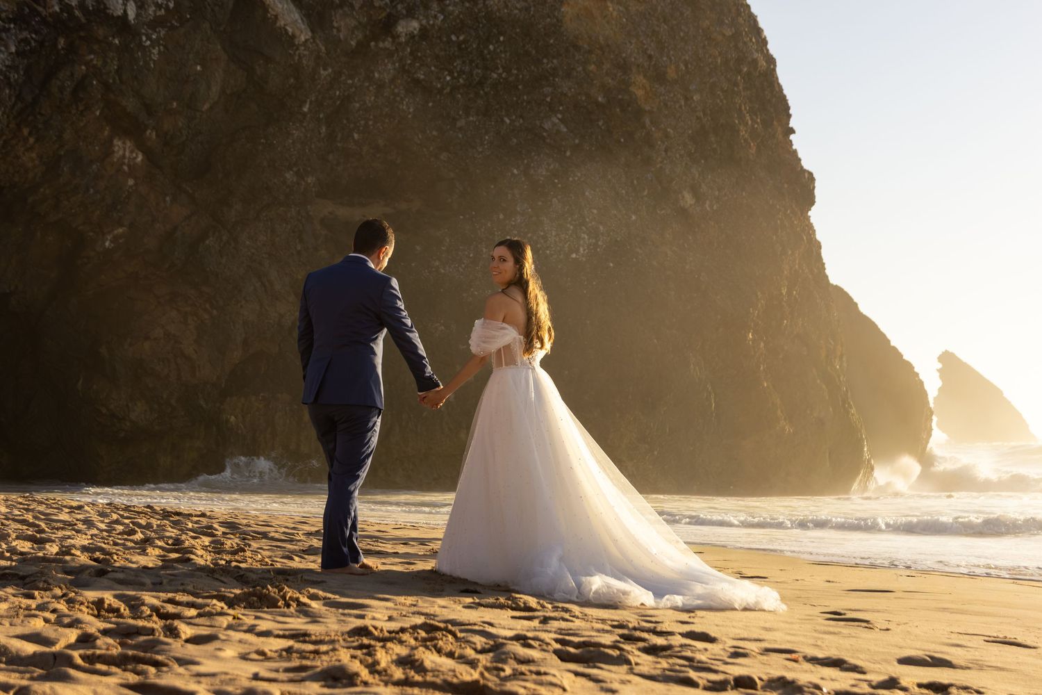 Wedding couple poses near dramatic coastal rock formations at sunset.