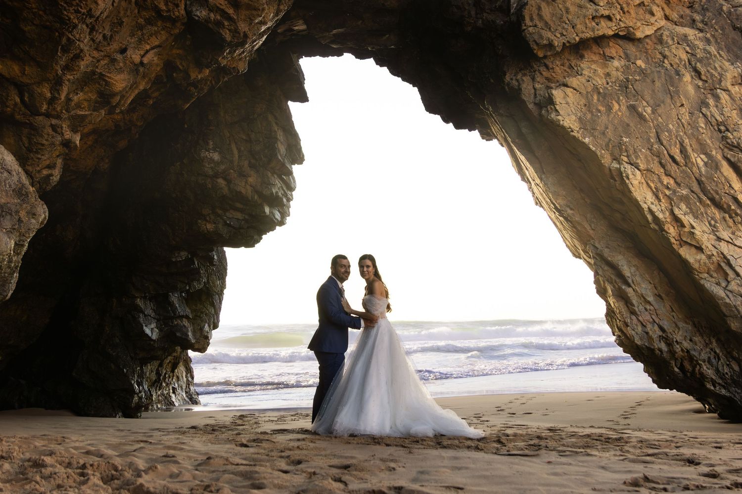 Wedding photos under a natural rock arch formation on the beach.