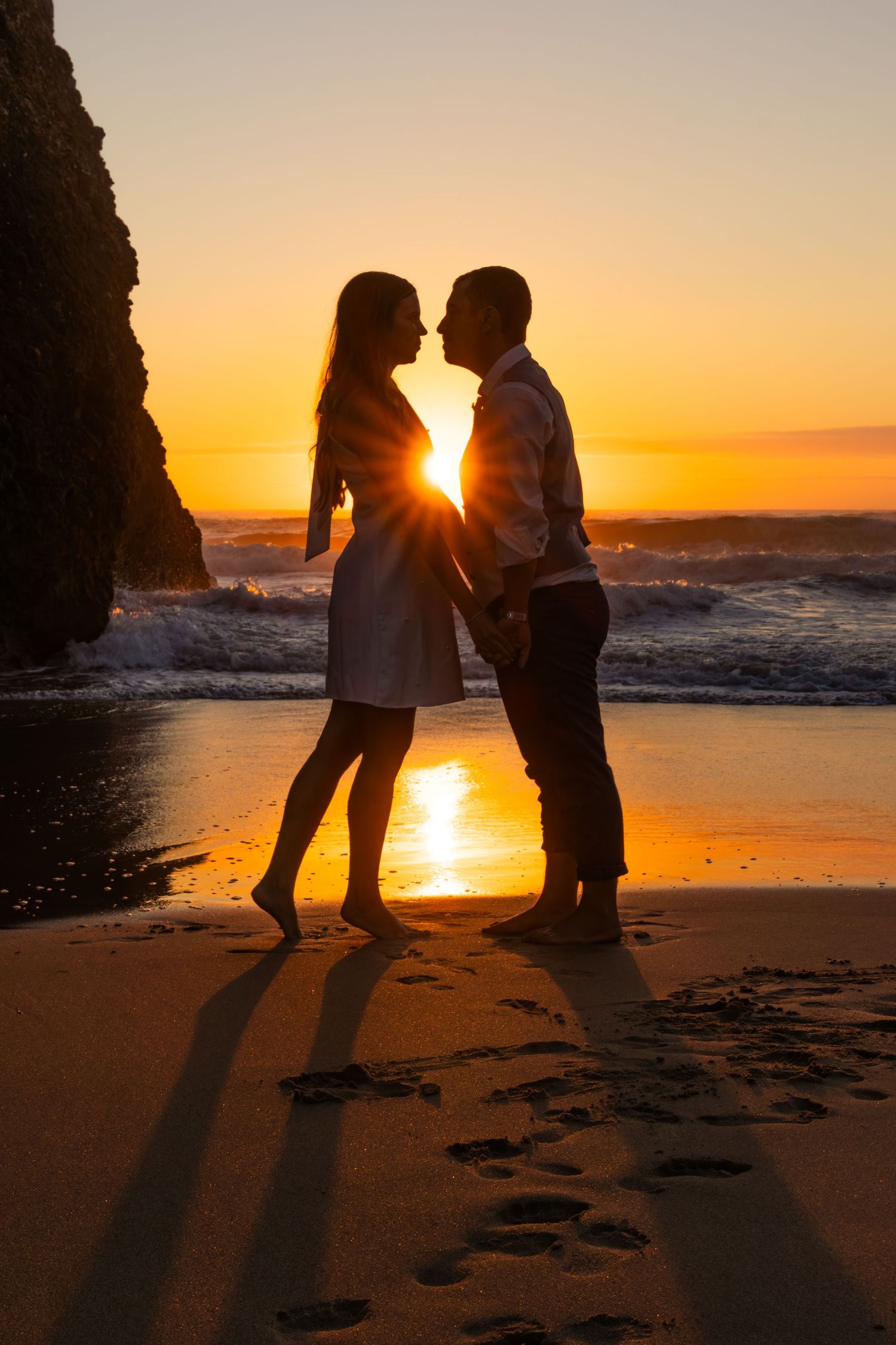 Silhouettes of a couple on beach at sunset with golden light streaming between them.