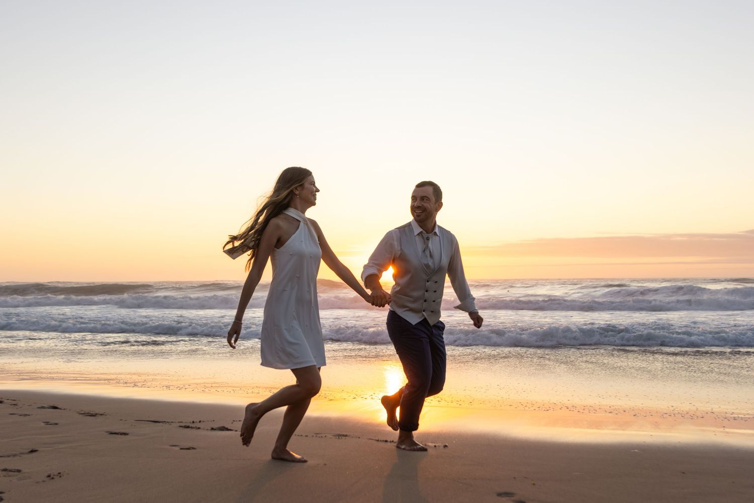 Romantic couple walking and playing on sandy beach during golden hour.
