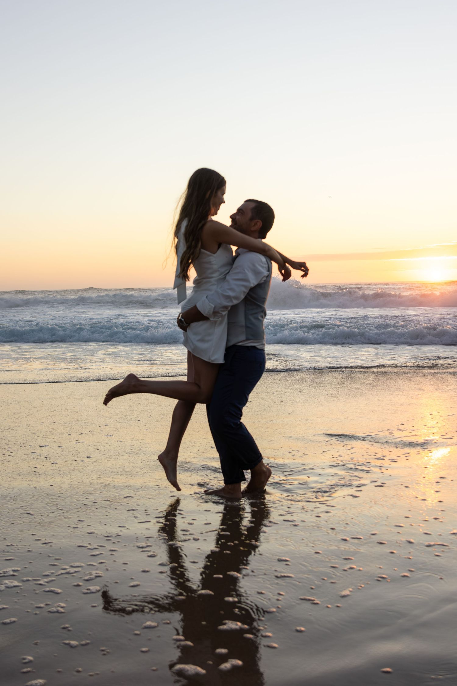 Playful couple splashing in ocean waves during sunset at the beach.