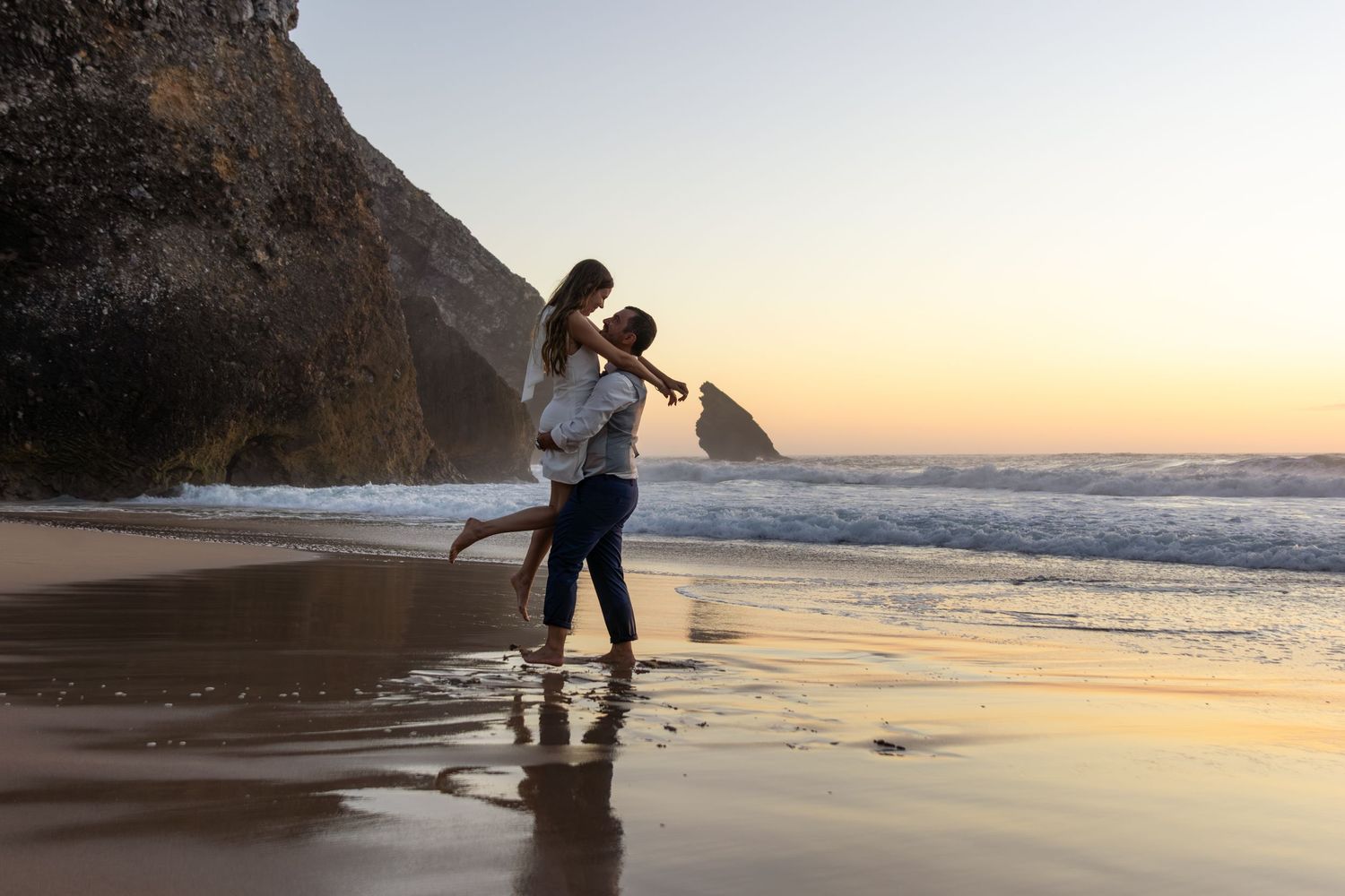 Couple dancing and embracing on sandy beach during golden sunset.