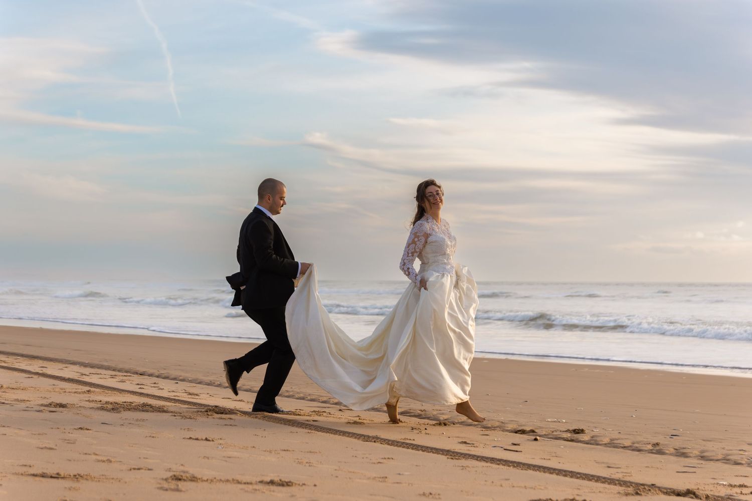 Couple walking along beach shore with flowing dress and veil.