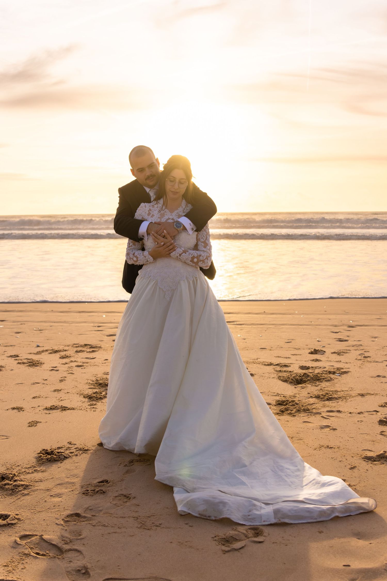 Newlyweds posing playfully on sandy beach at sunset.