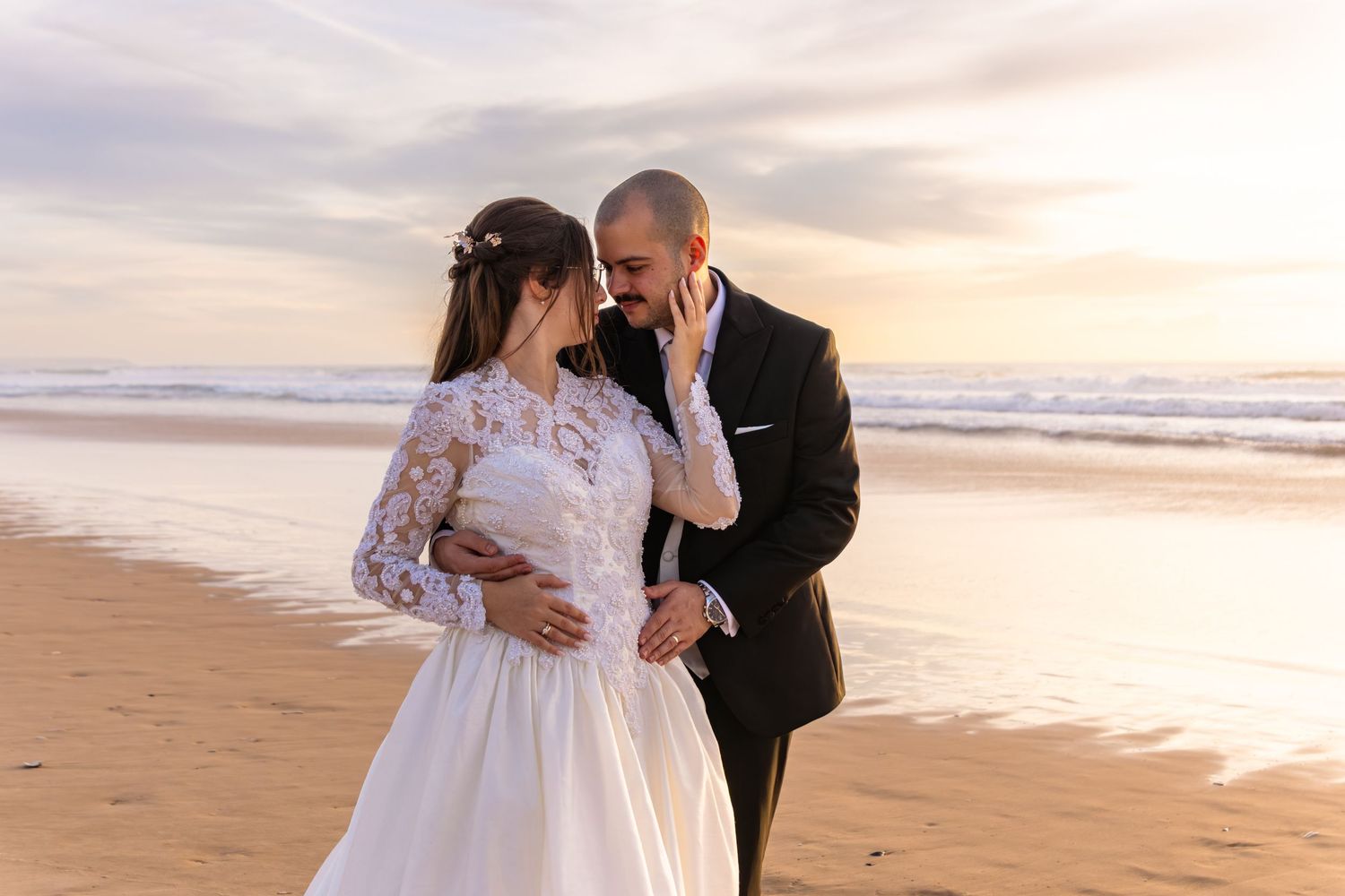 A couple in wedding attire embraces on a beach during golden hour photography session.