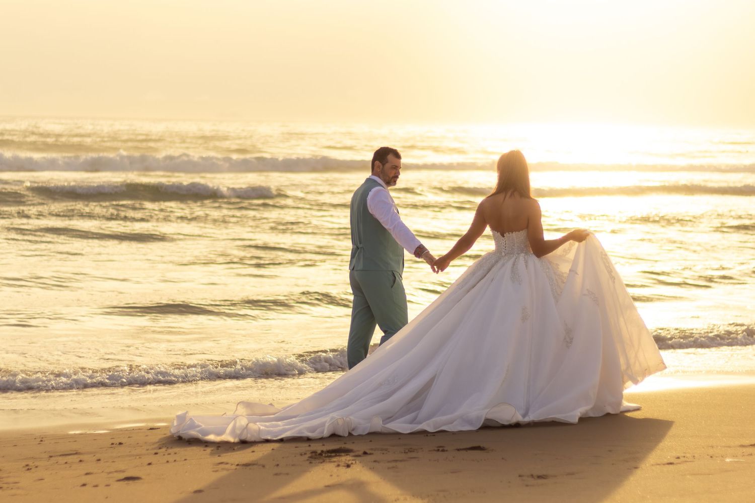 A wedding couple walks along a beach at sunset creating romantic silhouettes.