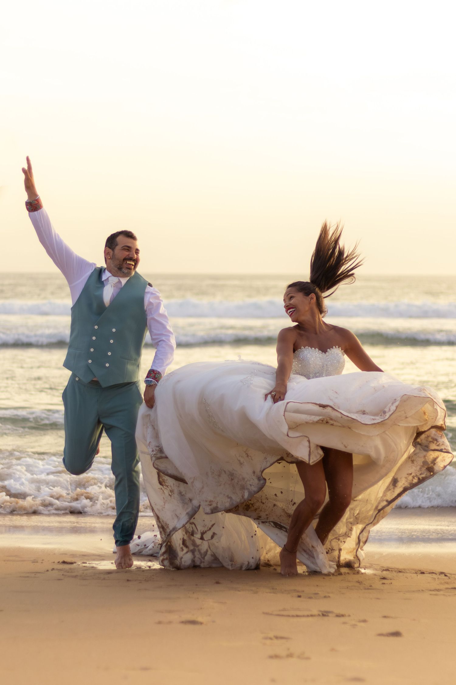 Playful beach wedding photos with flowing dress movements at golden hour.