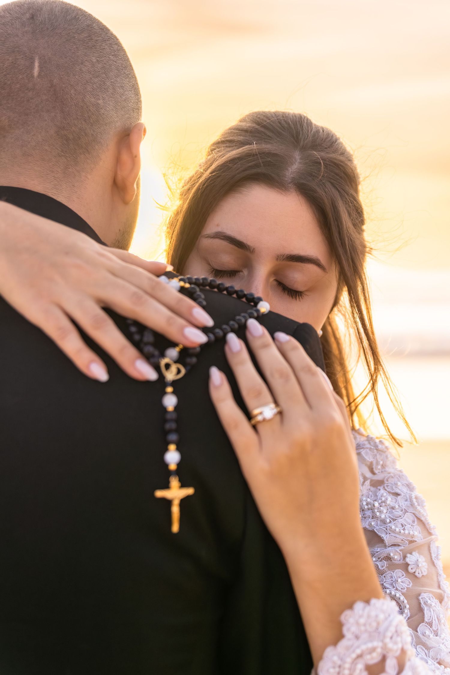 Close-up details of a bride's lace dress and jewelry during an emotional beach wedding moment.