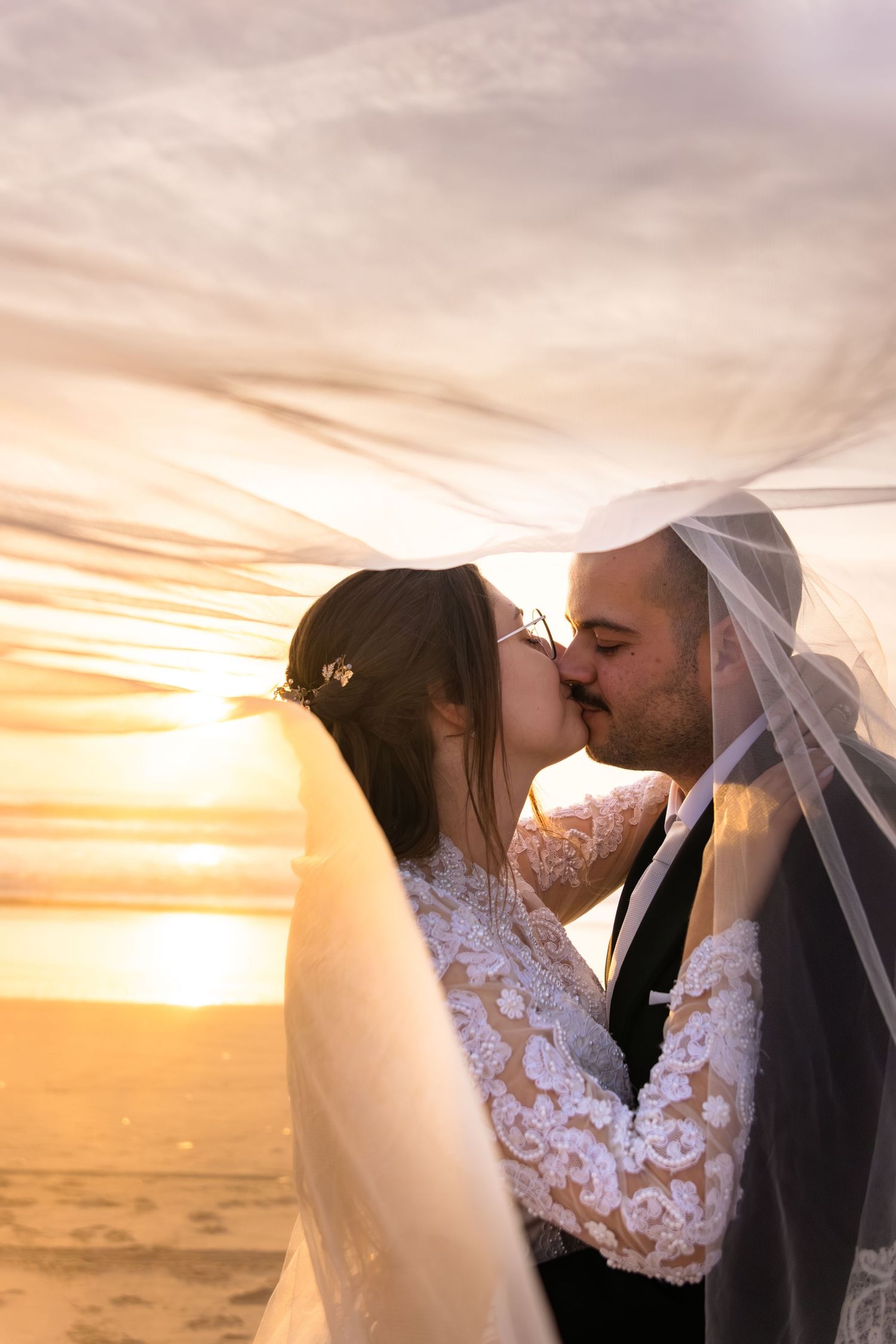 Artistic wedding photography captures intimate moments between newlyweds against a dramatic sunset sky.