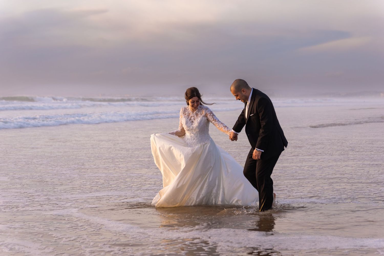 Wedding couple poses in shallow ocean water during sunset beach photography session.