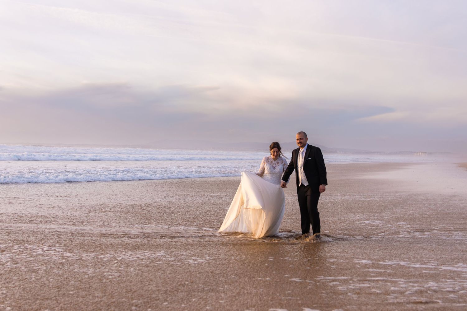 Wide angle beach wedding photography showing couple against dramatic coastal landscape.