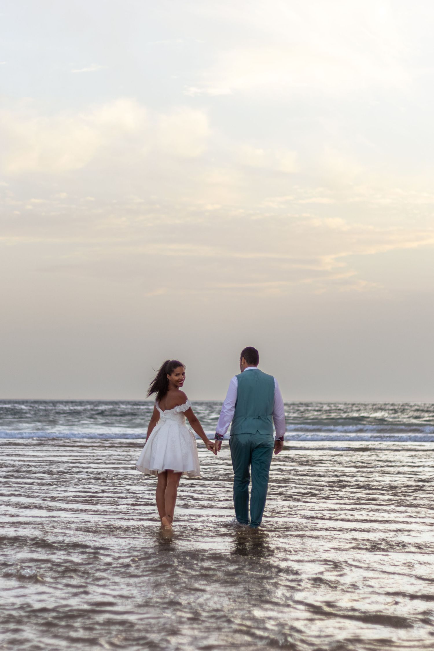 Couple wading through ocean water together during golden hour.