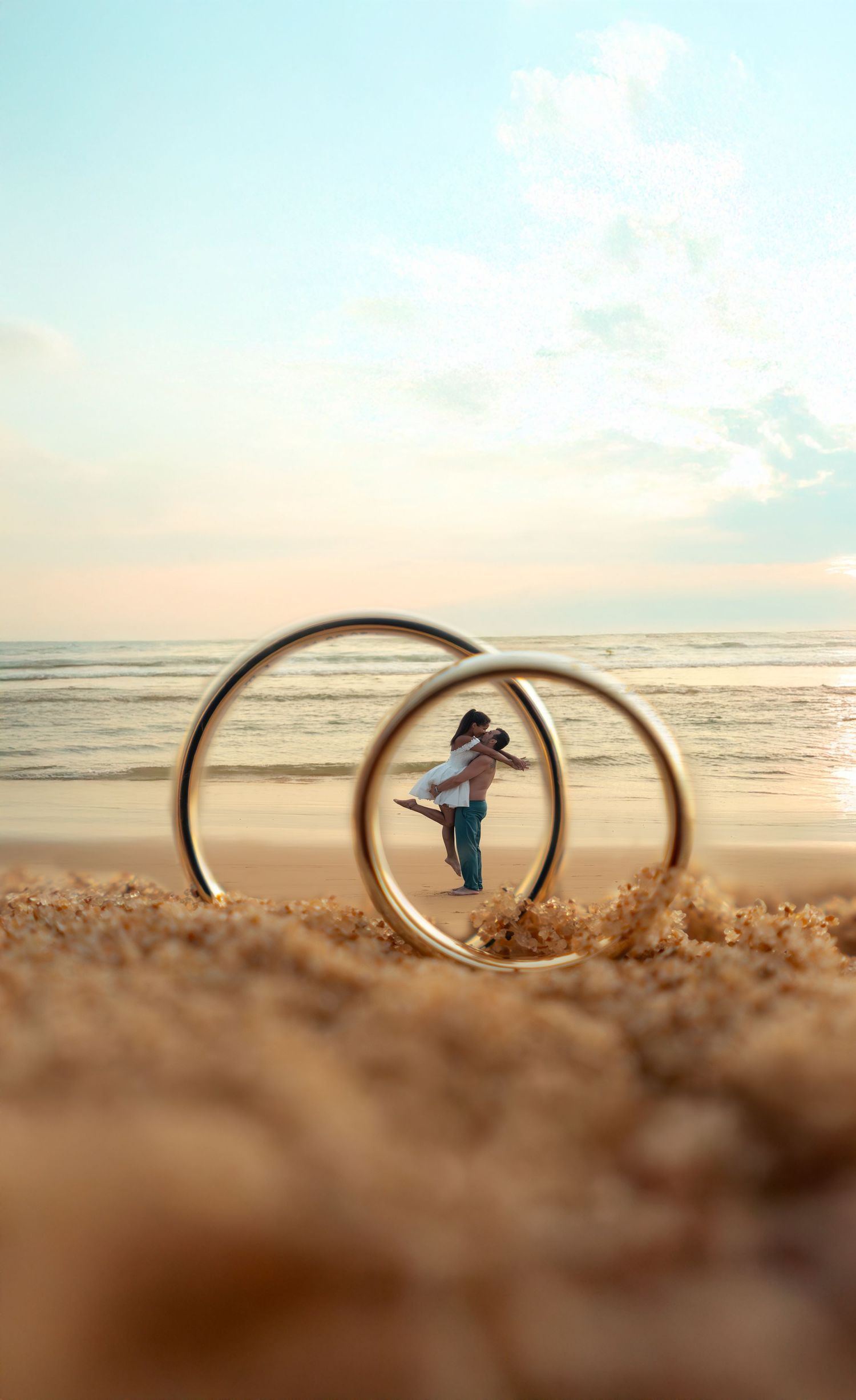Creative wedding ring photo showing couple through rings placed in beach sand.