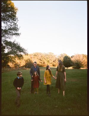 A group of people standing together in a grassy field at sunset with trees in the background.