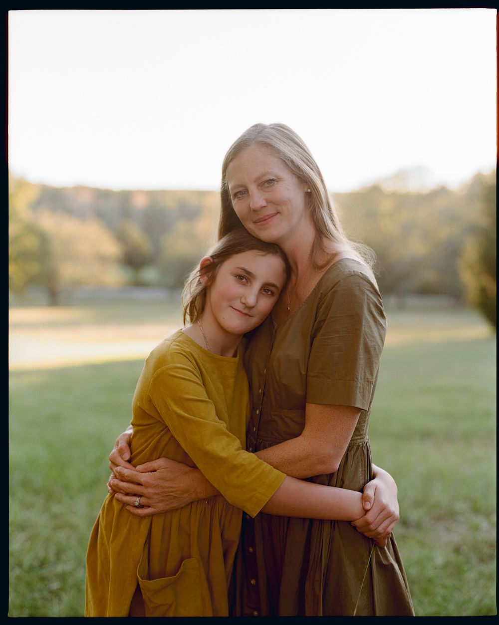Two figures embrace in a sunny outdoor field during golden hour, creating a warm and intimate moment.