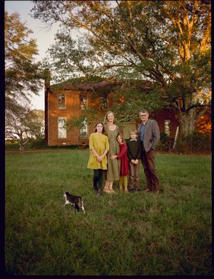 Rural family portrait in front of historic brick farmhouse at sunset with a cat in the foreground.