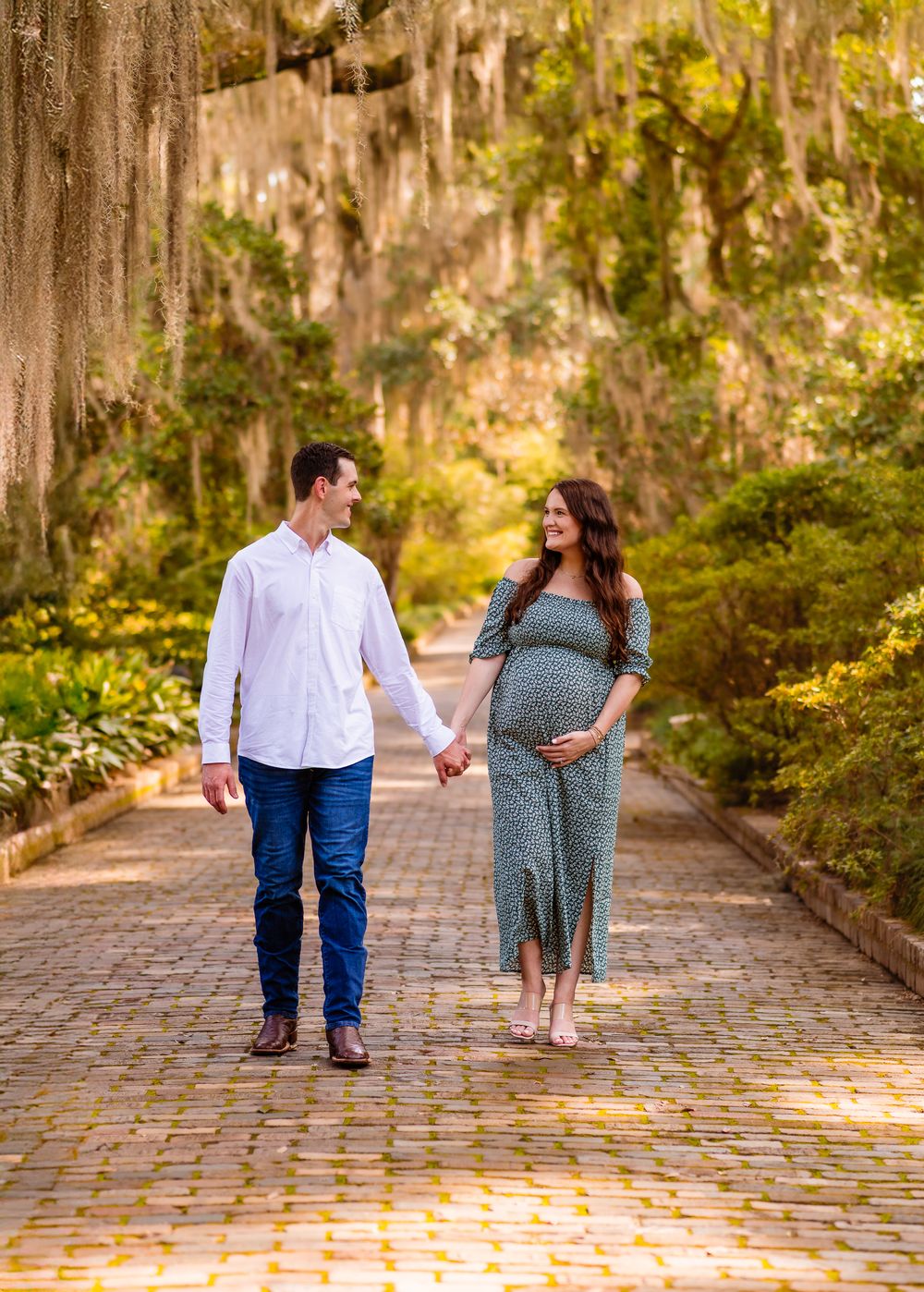 Couple walking hand in hand down a romantic cobblestone path lined with Spanish moss draped trees.