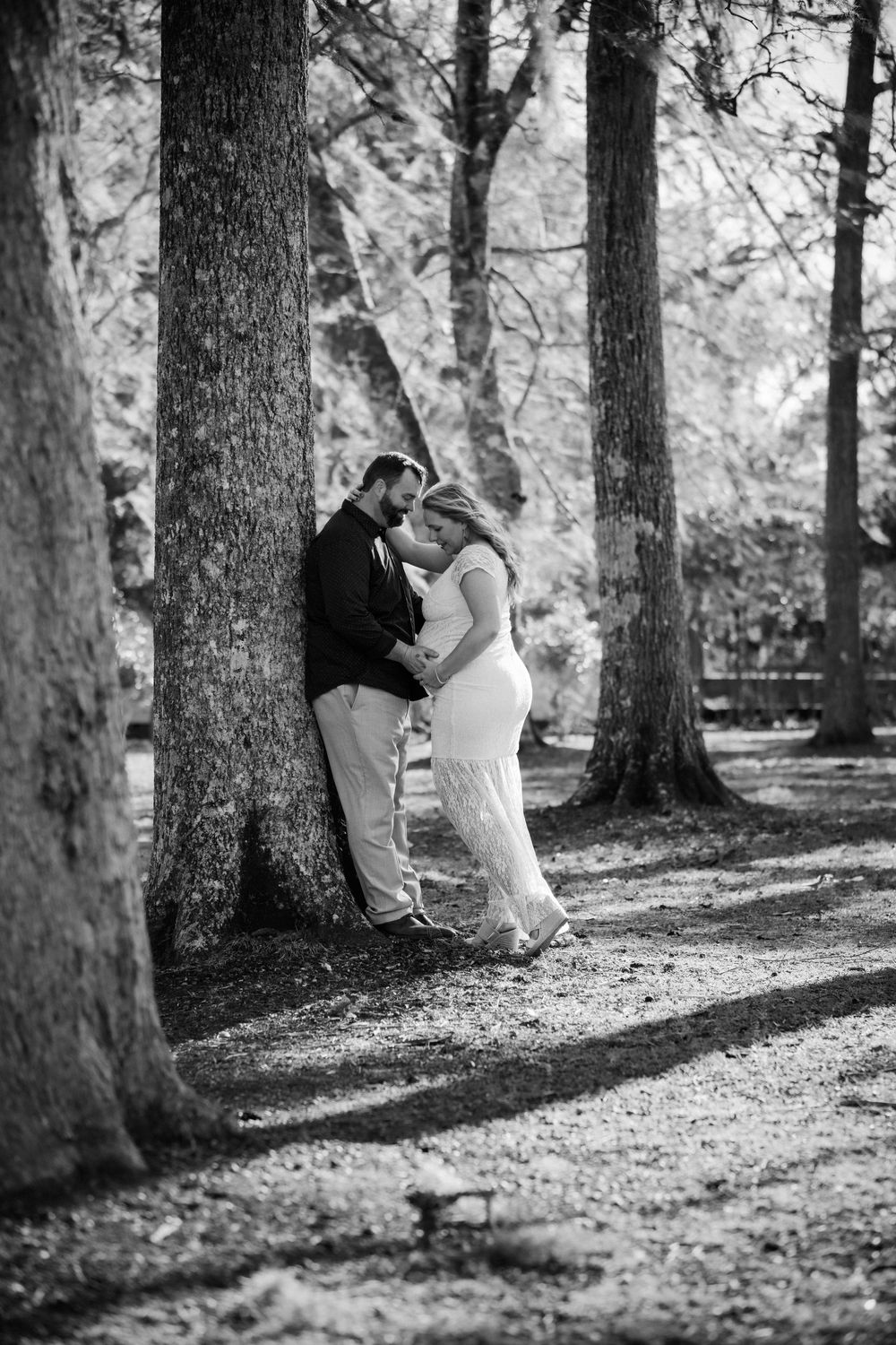 Black and white romantic photo sequence showing a couple in a wooded park setting with dappled sunlight through trees.