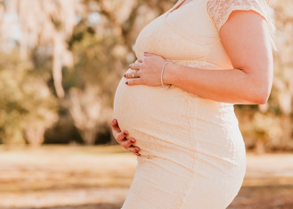 A pregnant woman in a white dress cradles her belly during a golden hour maternity photoshoot outdoors.