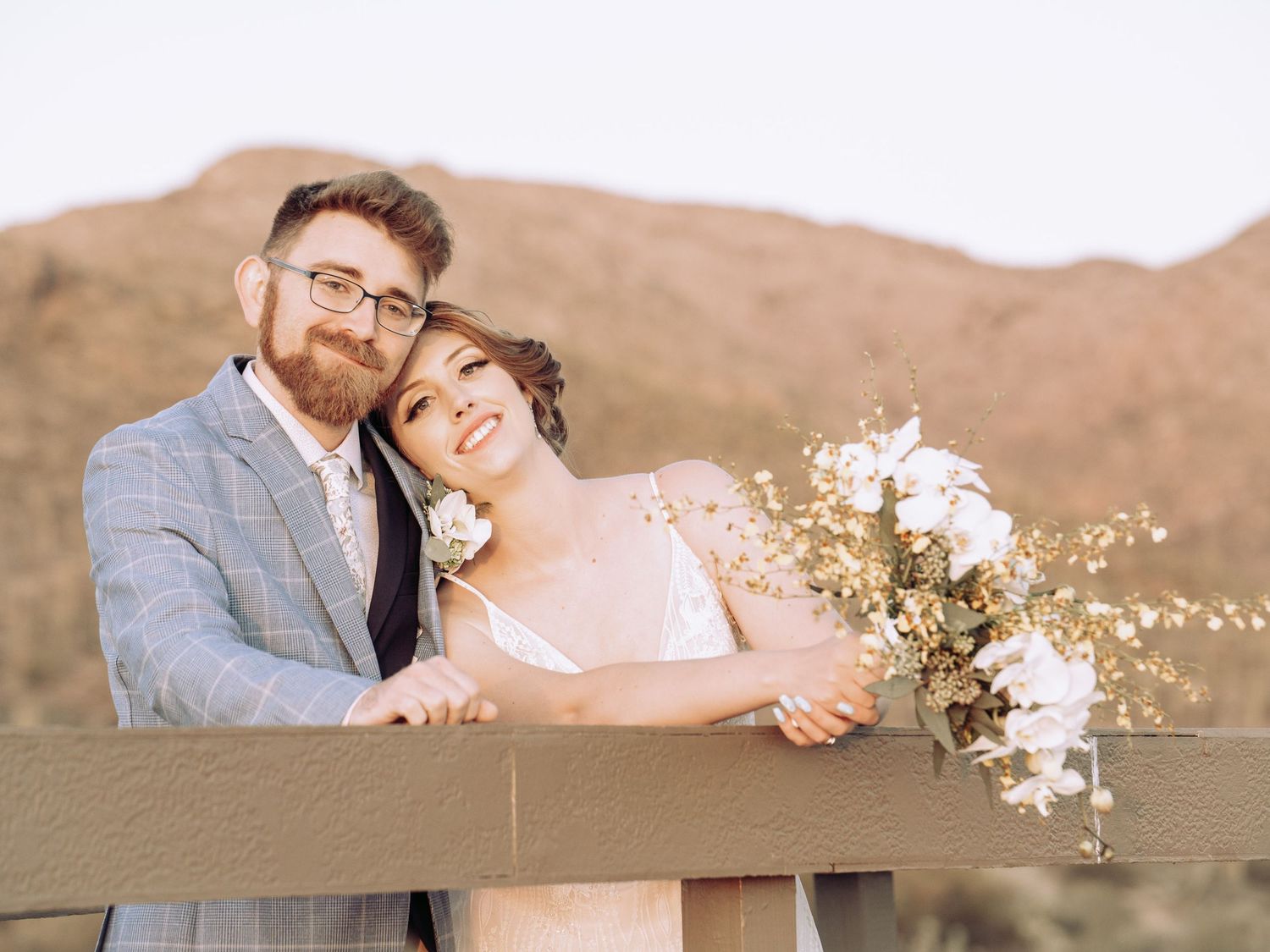 Couple posing with floral bouquet against desert mountain backdrop during sunset.