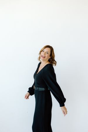 Dynamic pose in a black dress with billowing sleeves against white backdrop.