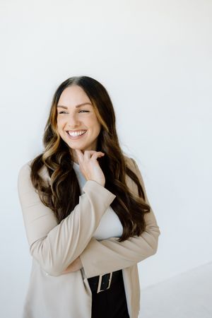 Professional portrait of someone in a beige cardigan and black pants against a white background with a warm smile.