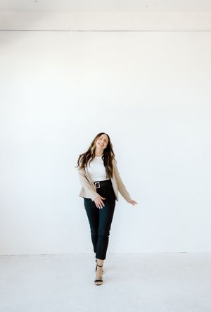 Casual lifestyle photo showing movement in a beige cardigan and black pants against white.