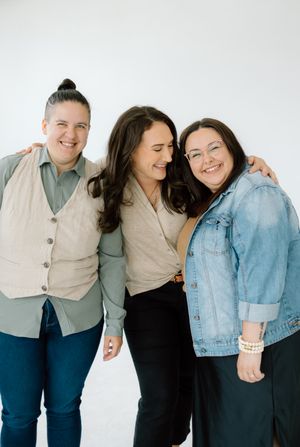 Three friends share a joyful moment against white backdrop wearing casual attire.
