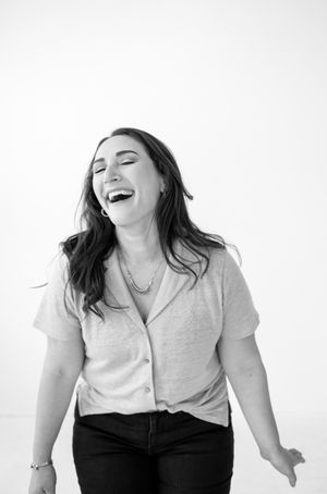 A candid black and white portrait of a joyful person laughing with eyes closed while wearing casual attire.