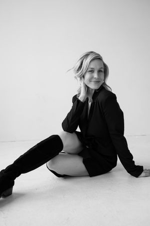 Black and white portrait in stylish black outfit and boots against white floor.