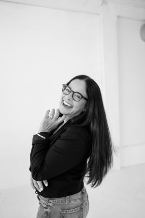 A black and white photo showing someone in glasses and dark clothing laughing expressively.