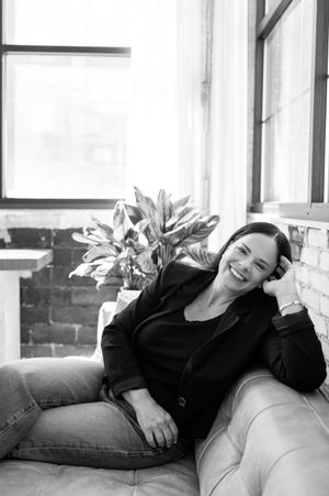 A black and white portrait of someone lounging on a couch with decorative plants in the background.