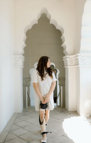Woman in white dress poses under ornate archway with scalloped details.