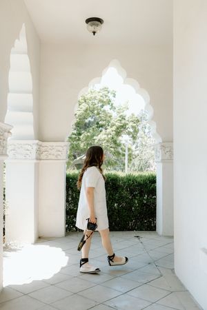 Woman walking through white arched corridor with decorative columns.