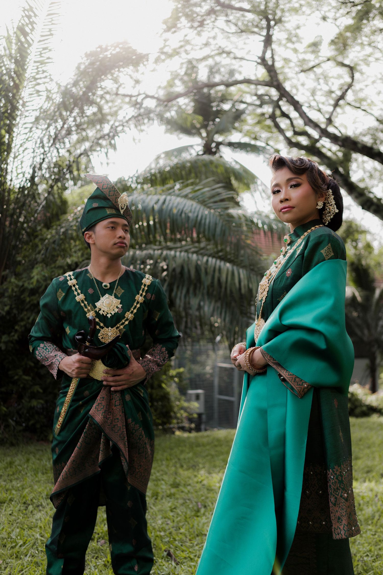 Two people in traditional attire sitting together on a grassy hillside.