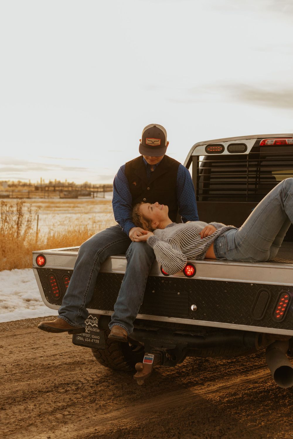 Western couple relaxing on truck tailgate during golden hour in rural Idaho setting.