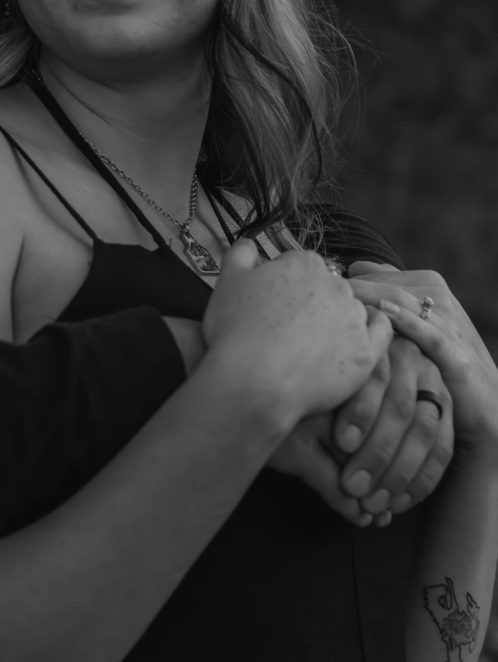 Black and white close-up of interlocked hands with visible tattoos.
