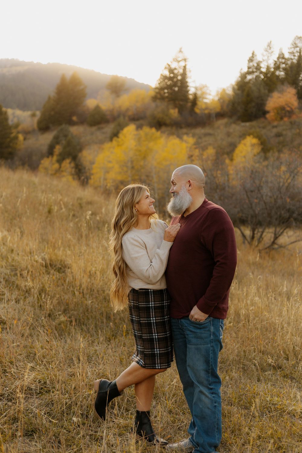 Romantic couple portrait in golden autumn field with mountain backdrop at sunset.