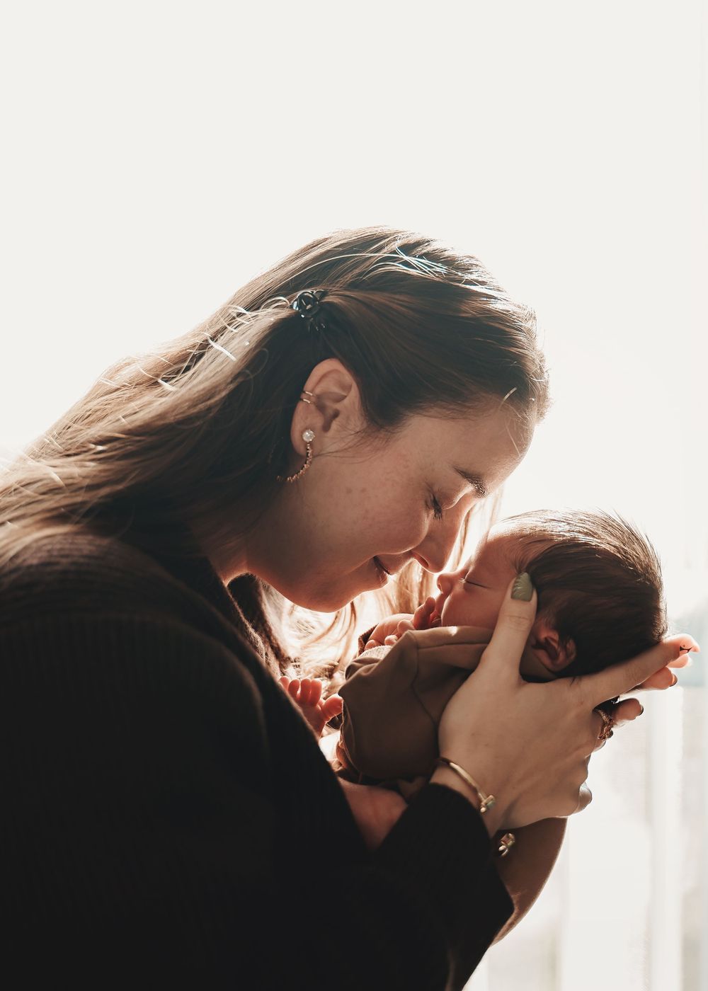 A tender silhouette moment between parent and child as sunlight streams through a window creating a warm backlit glow.