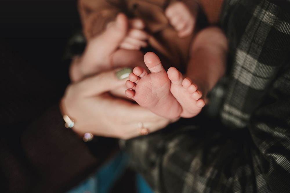 A small baby's feet being gently held in loving adult hands against a dark background.