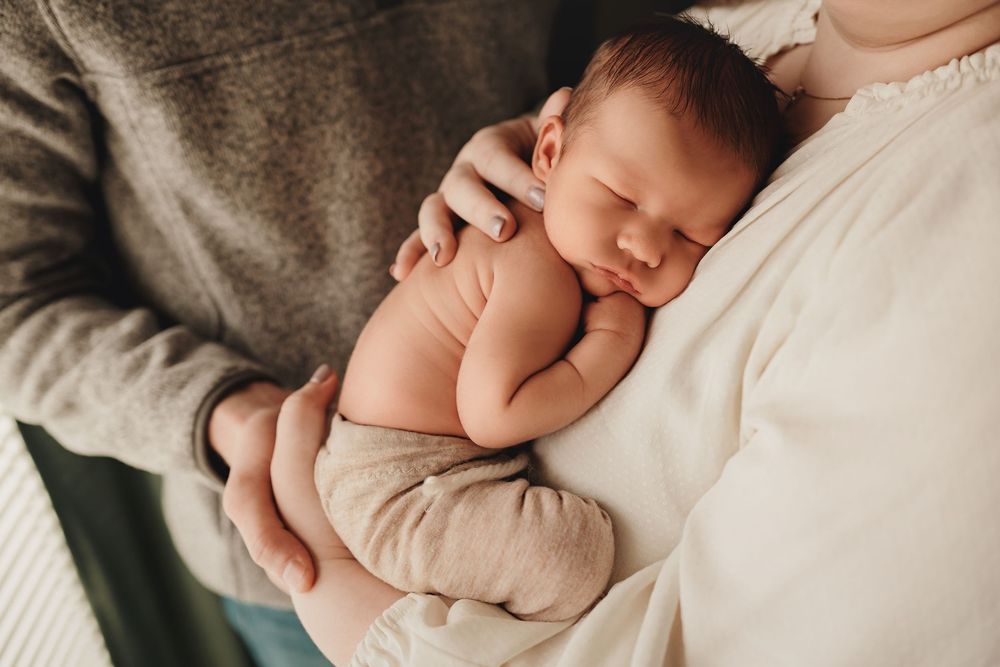 Newborn baby sleeping peacefully while wrapped in soft beige swaddle blanket against neutral backdrop.