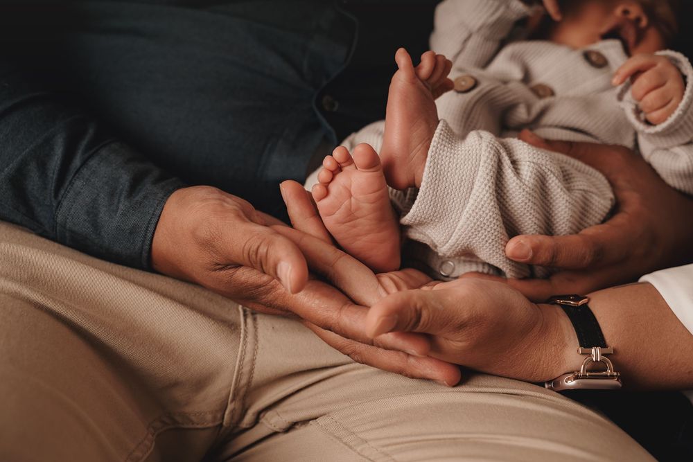 Adult hands gently hold tiny baby feet against beige background in intimate close-up moment.