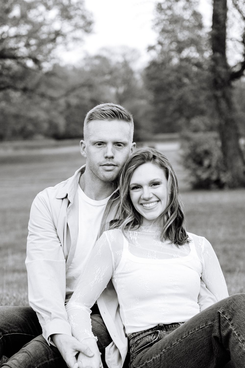 A black and white outdoor portrait of a smiling couple in casual attire.