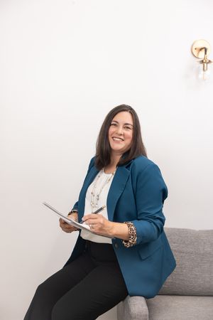 female bookkeeper in Bellevue, WA sitting on couch arm writing in notebook smiling wearing teal blazer for branding business headshot