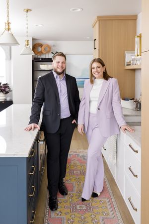 husband & wife real estate couple in Bellevue, WA standing in kitchen wearing power suites smiling for lifestyle branding photo