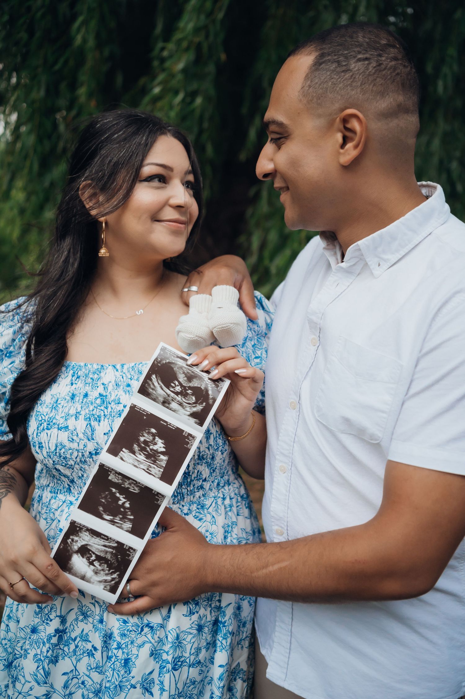 Happy couple holding ultrasound photos and tiny baby shoes during an outdoor pregnancy announcement photoshoot.