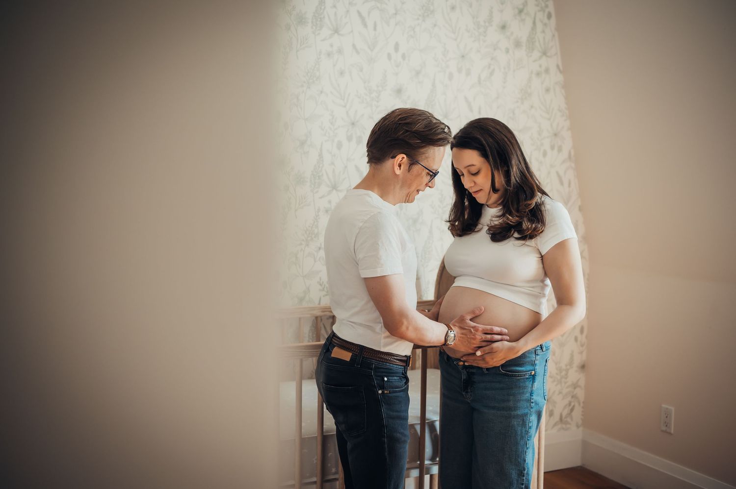 Couple tenderly cradling pregnant belly during maternity photo session indoors.