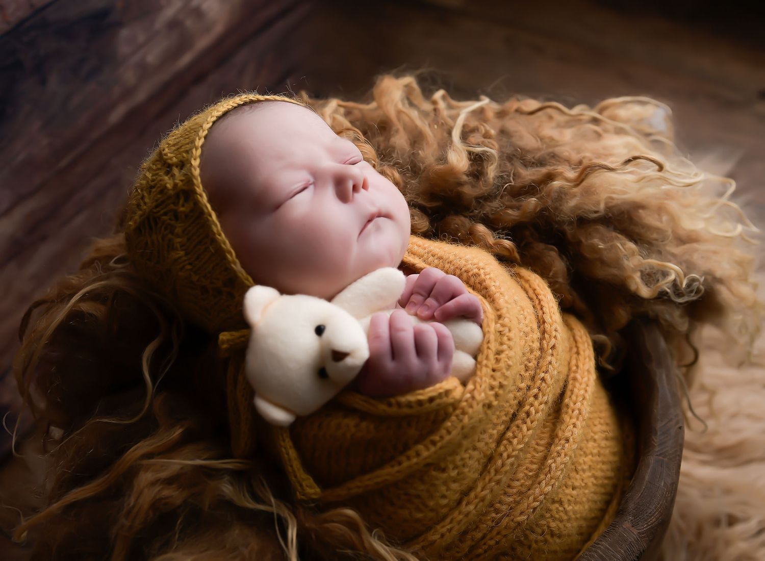 Newborn baby holding the teddy while laying on a fluffy blanket. The colours and autumnal with a contrast of shadows.